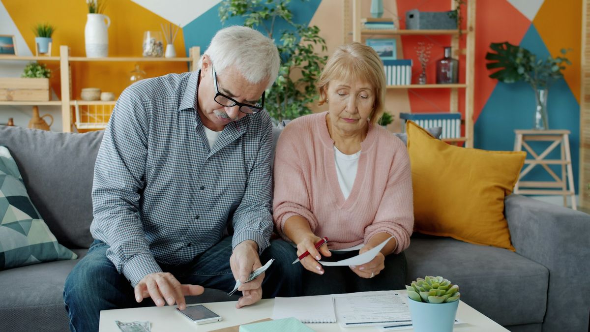 Older couple sitting on a sofa reviewing paperwork and a calculator together