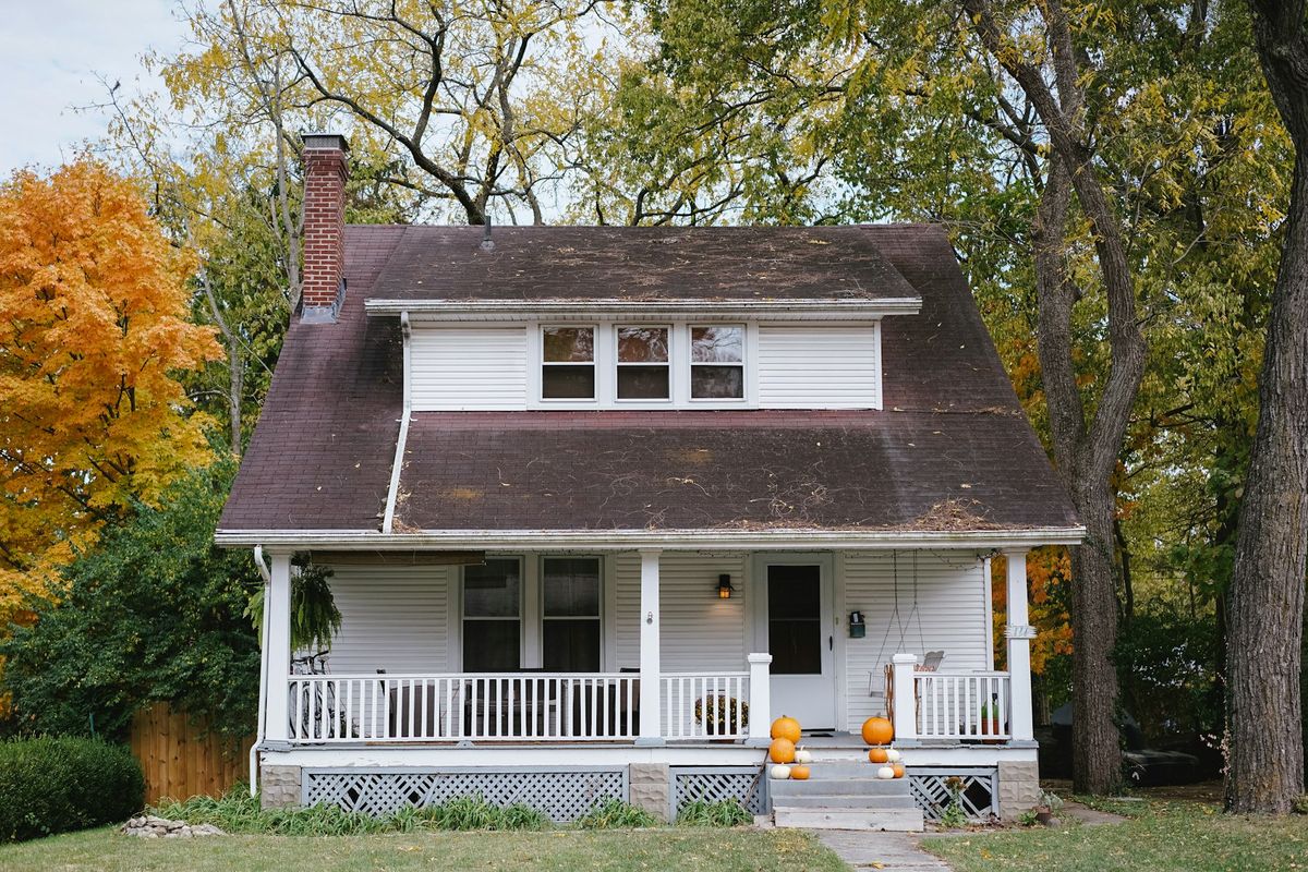 White two-story house with a front porch surrounded by autumn trees